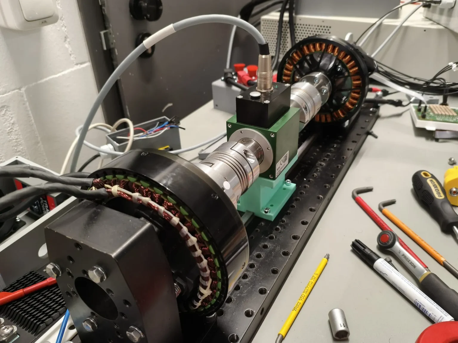 Test bench at Persystems in Regensburg: outrunner motor and load machine coupled through a torque transducer, tools on the measuring bench beside it