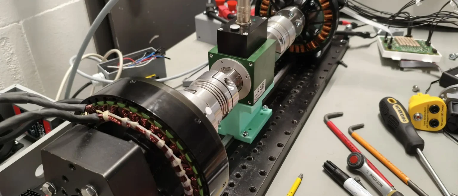 Test bench at Persystems in Regensburg: two outrunner motors connected through couplings and a torque transducer, mounted on the perforated plate of the measuring bench